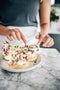 vanilla shortcrust pastry base, filled with a white chocolate, orange mascarpone cream, towered with white chocolate shards garnished with slithered pistachios and edible red rose petals and grated with orange zest.